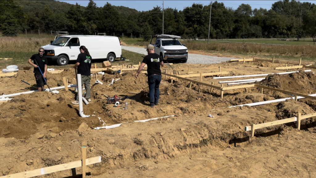 Plumbers preparing trench for underground sewer system installation.
