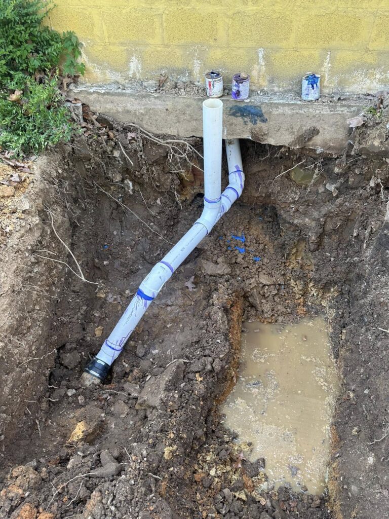 Exterior sewer pipe repair with new PVC line installed at home foundation.